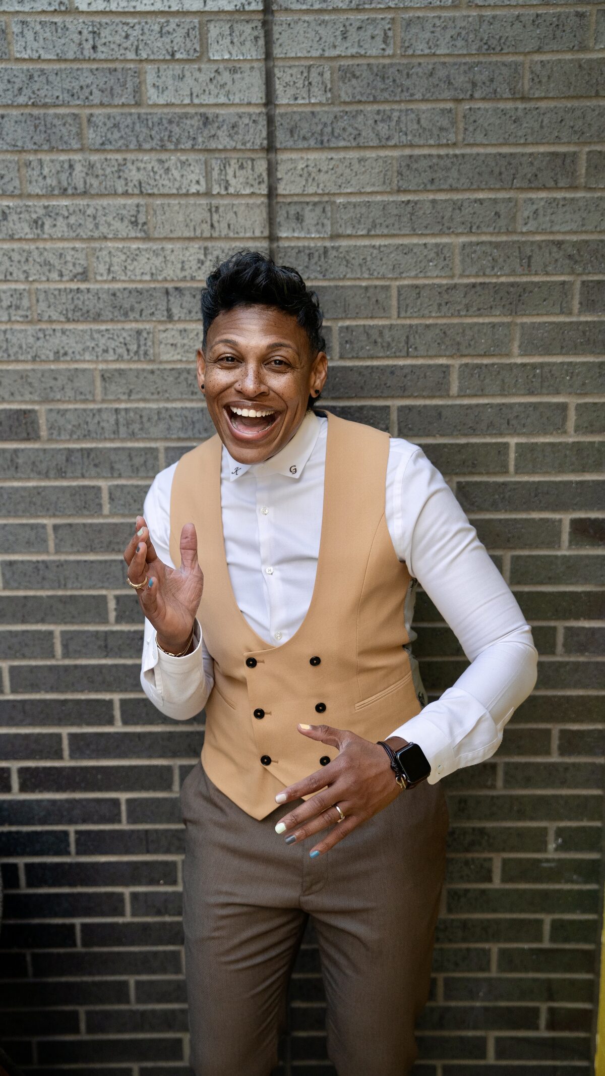 Khaliah O. Guillory laughing in a tan vest and white shirt against a brick wall