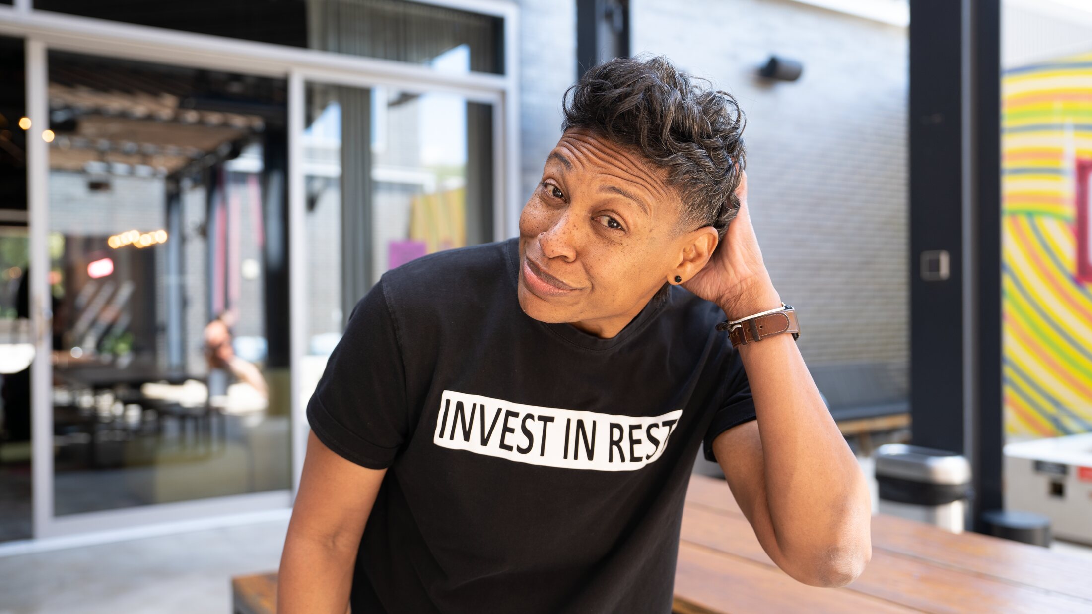 Khaliah O. Guillory resting her head on her hand, wearing an INVEST IN REST t-shirt