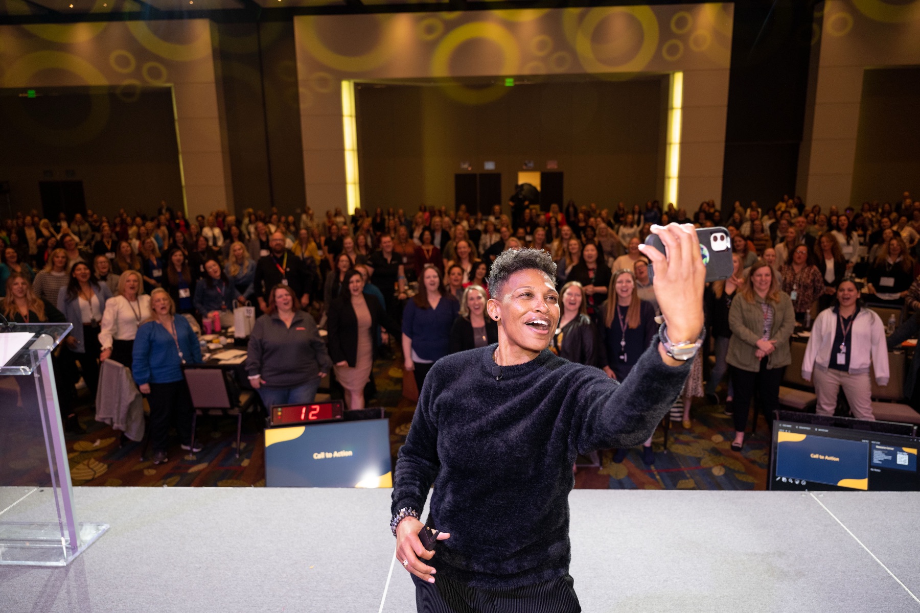 Khaliah O. Guillory on stage taking a selfie with a packed audience behind her