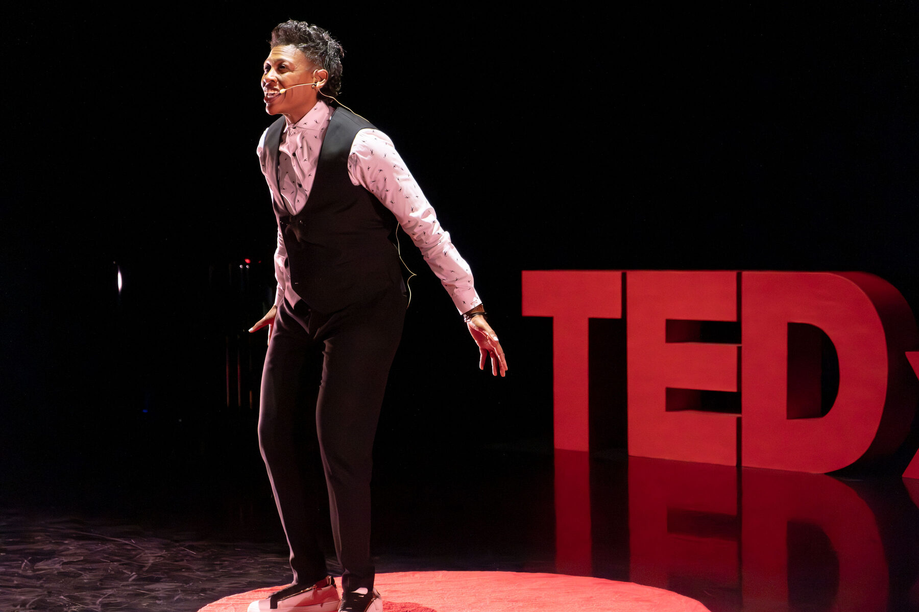 Khaliah O. Guillory on the TEDx stage, leaning toward the audience beside the red TEDx letters
