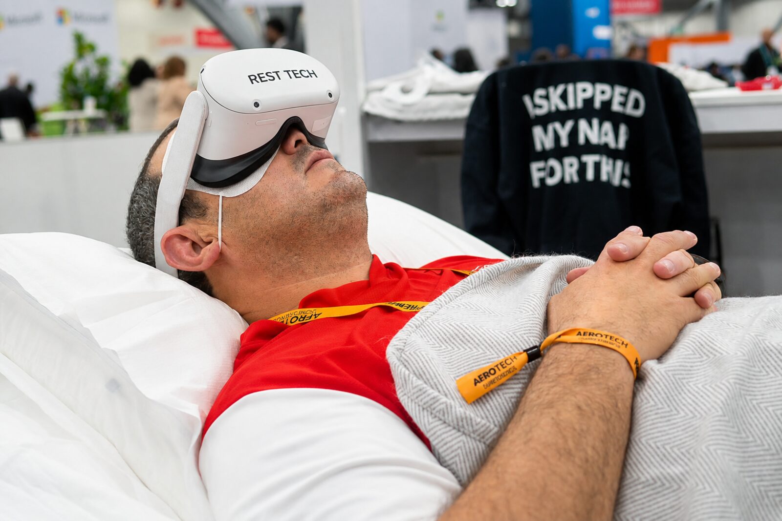 A participant reclining with hands clasped, wearing a Rest Tech branded VR headset on the exhibition floor.