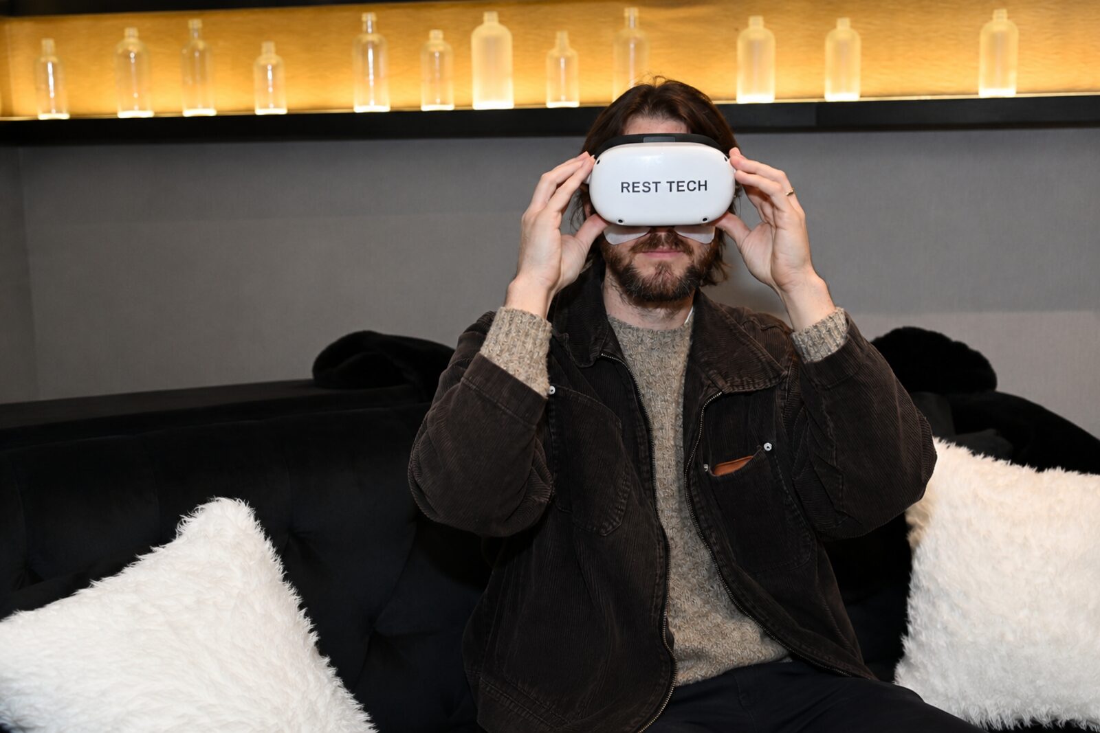 A guest settling back on a couch and lowering a Rest Tech VR headset over their eyes.