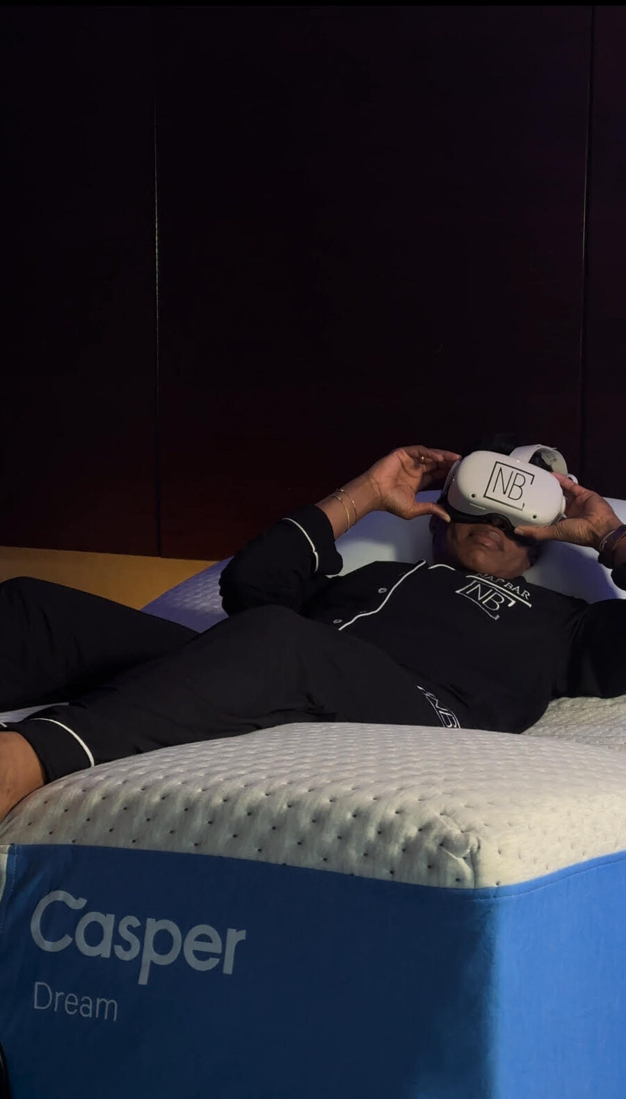 A participant reclining on a zero-gravity Casper bed, lowering a Nap Bar VR headset over their eyes.