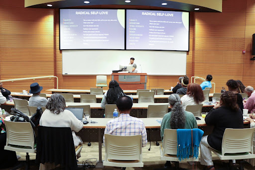 Workshop participants seated in a room facing a facilitator and presentation screens.